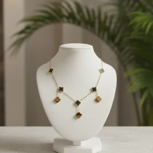 Long gold-toned necklace featuring multiple clover motifs in black, white, and brown Tiger Eye-look stones, displayed on a white jewelry bust.